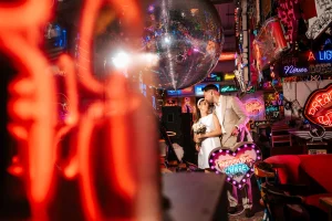 Pre-wedding portrait of couple bathed in warm neon light surrounded at Gods Own Junkyard, London pre wedding shoot